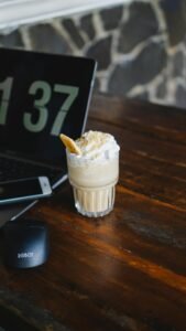 Cozy workspace featuring a creamy iced coffee and modern laptop setup on rustic wooden table.