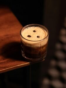 A refreshing espresso martini topped with coffee beans on dark wooden surface, perfect for cocktail enthusiasts.