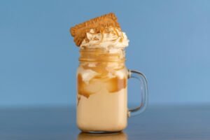 A creamy caramel milkshake topped with whipped cream and a biscuit, perfect for a sweet treat.