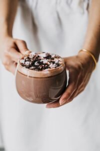 A person holds a cup of hot chocolate topped with marshmallows and cocoa sprinkles.